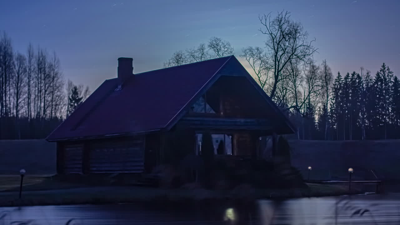 Statische Zeitraffer-Ansicht des Sonnenaufgangs über einem See vor einer Holzhütte am frühen Morgen