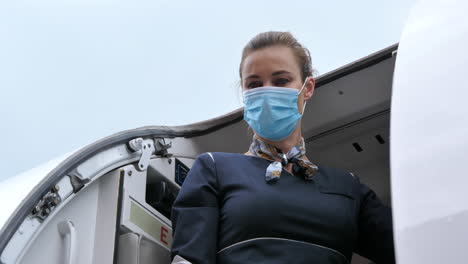 flight attendant with coronavirus protection mask closes aircraft door