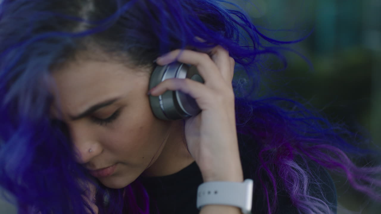retrato de una hermosa mujer joven sonriendo feliz se pone auriculares escuchando música disfrutando de un estilo de vida relajado el viento soplando el cabello púrpura de cerca