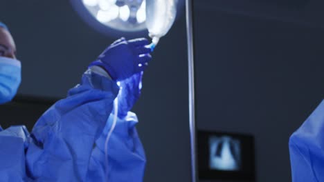 médicos con ropa de protección y máscaras faciales preparando al paciente para la cirugía en el quirófano
