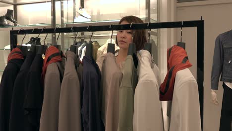 happy asian woman looking at clothes rack in fashion shop