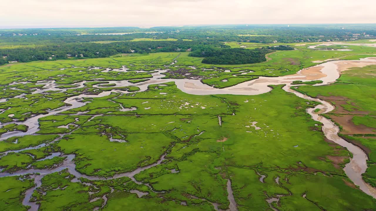 Expansive marsh system captured in aerial view shows tidal waterways winding through lush grasses, reflective pools dotting the surface, and natural shapes spreading across the horizon