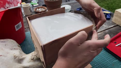 artisan's hands shaping clay mould on a wooden framed head bust around drying plaster - close up handheld