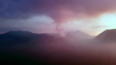 Drone-view-of-the-Bromo-volcano-at-dusk,-with-smoke-and-clouds