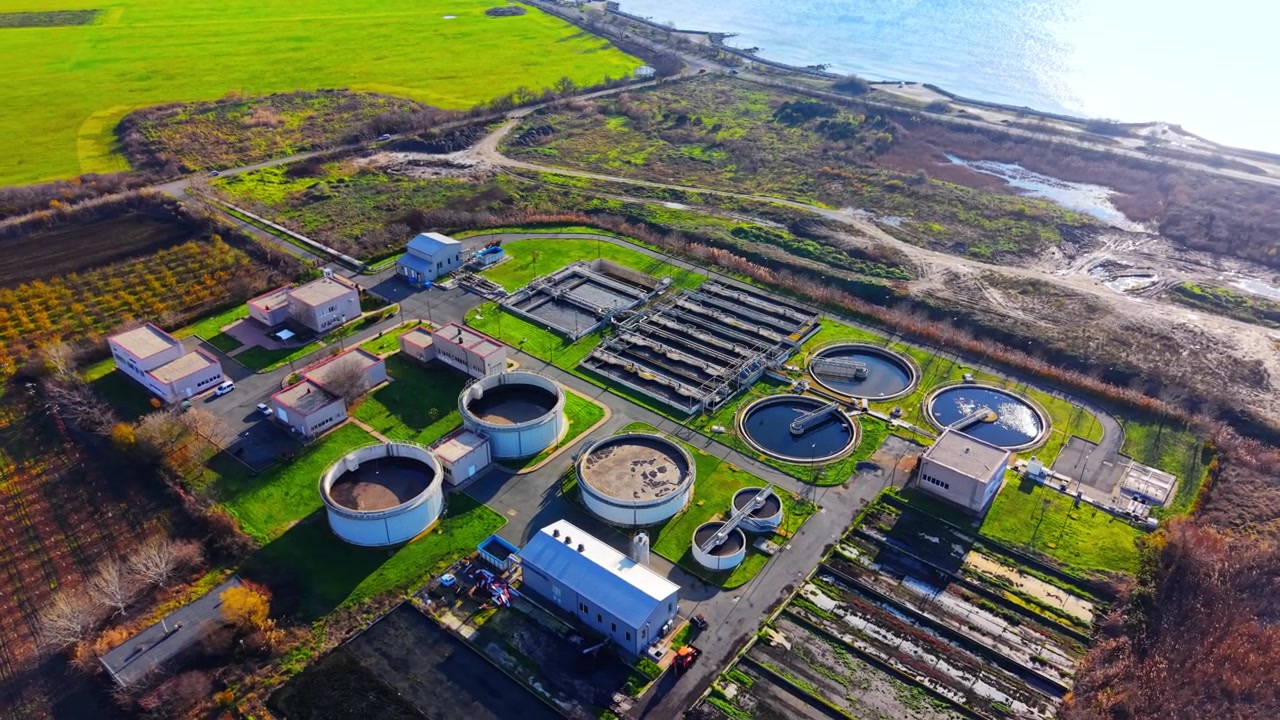 Wide elevated perspective showing industrial processing facility situated along the coastal zone and green fields. Drone shot of water purification infrastructure near Pomorie, Bulgaria.