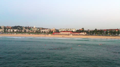 Drone-flying-over-the-ocean-at-Bondi-beach-as-morning-swimmers-swim-across-the-bay,-Sydney-Australia