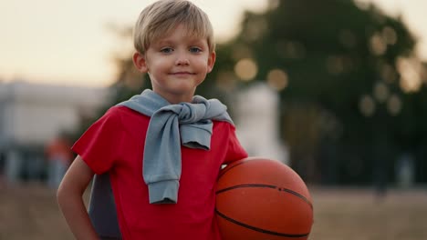 Porträt-Eines-Glücklichen-Kleinen-Blonden-Jungen-Mit-Blauen-Augen-In-Einem-Roten-T-Shirt-Mit-Einem-Basketball-Im-Park.-Glücklicher-Kleiner-Junge,-Der-Spaß-Hat-Und-Sportspiele-Im-Park-Spielt