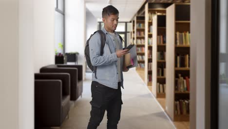 three quarter length shot of male university or college student looking at mobile phone in library