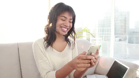 Mujer-Sonriente-Sentada-En-El-Sofá-Con-Su-Computadora-Portátil-Enviando-Mensajes-De-Texto