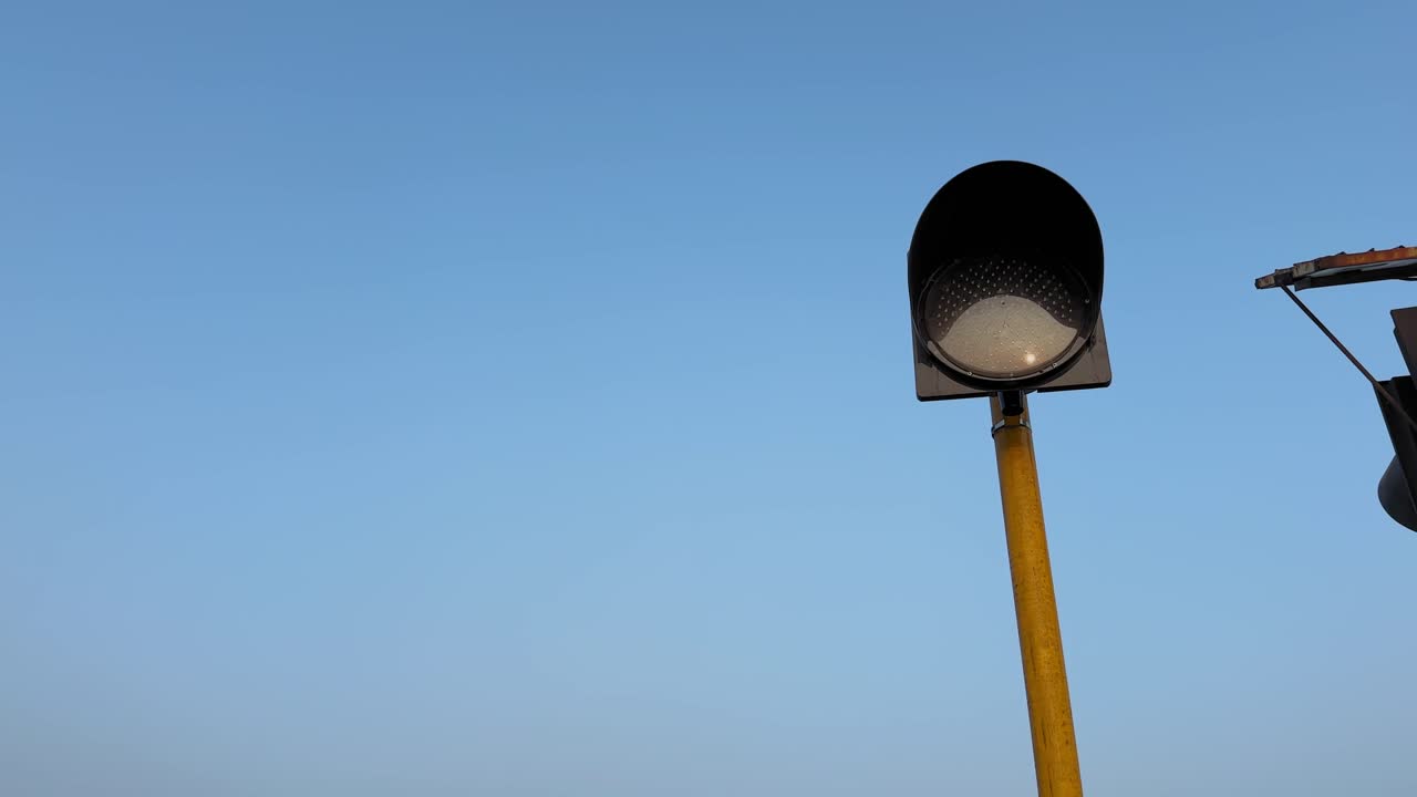 Statisk bild tagen i låg vinkel av en solcellsdriven blinkande trafikvarningslampa monterad på en hög stolpe, cirkulär lins riktad mot vägbanan mot en klarblå himmel som betonar trafiksäkerhetsanordningen