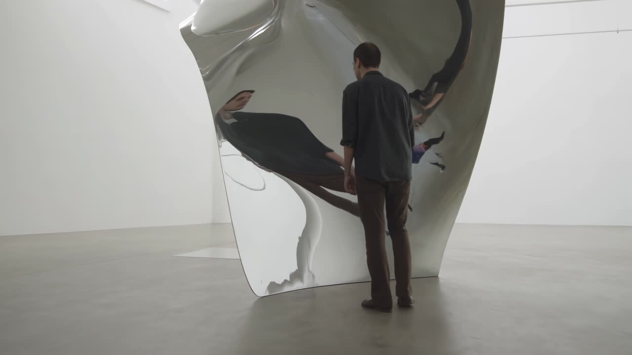Uomo cammina verso e osserva una grande scultura metallica riflettente in una galleria