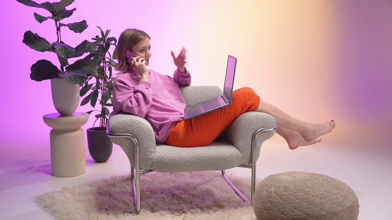 A woman lounges barefoot in a stylish armchair, balancing a laptop and phone call. Surrounded by soft tones, greenery, and a pastel gradient, this scene captures calm productivity and modern lifestyle