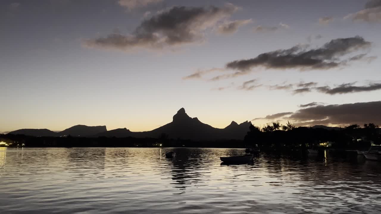 A calm and serene view of the Rempart Mountain early in the morning from over the water surface, passing local fishermen's boats.