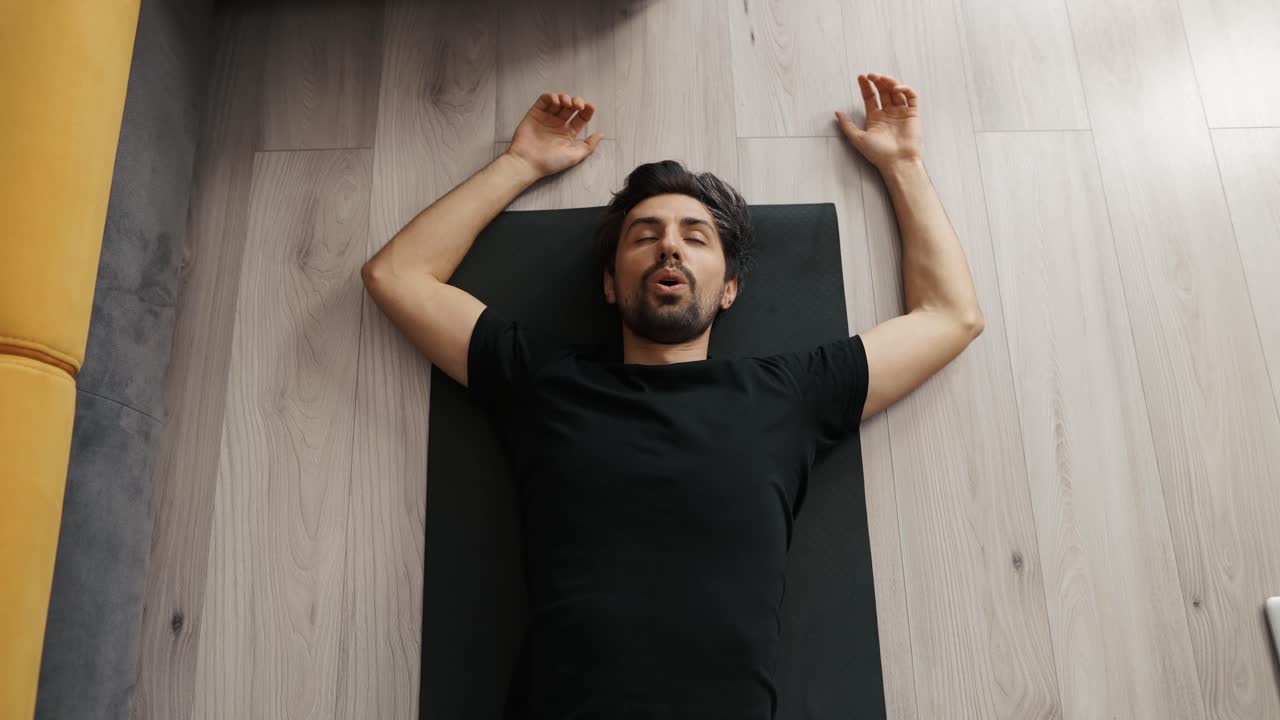 Tired exhausted man with wide spread arms lying on fitness on mat looking up