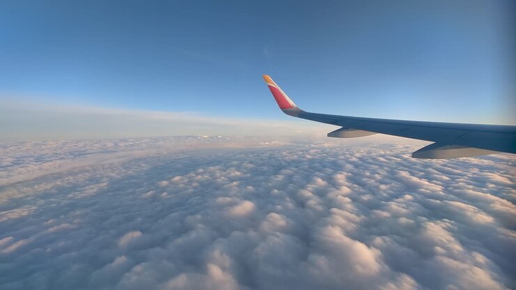 Udsigt fra flyvindue. Flyvinge svæver over et skyhav en solrig eftermiddag.