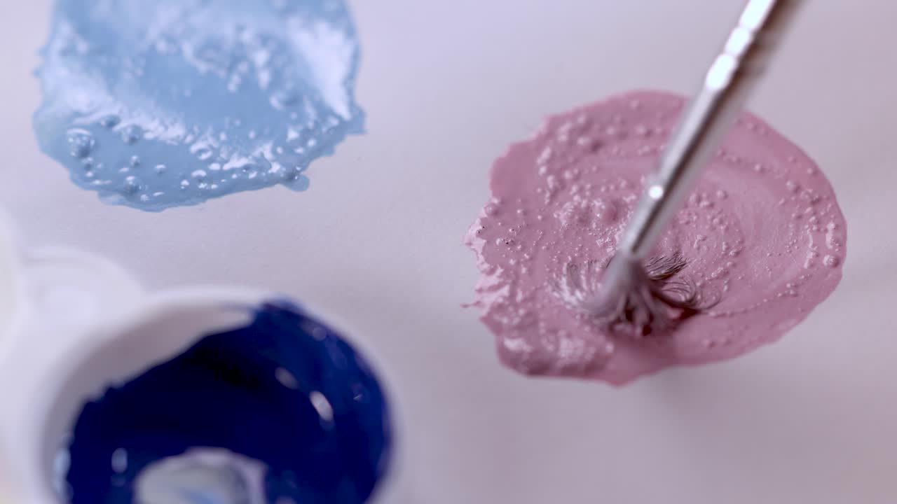 Artist mixes pink paint with brush in palette, soft lighting, macro close-up, smooth camera movement