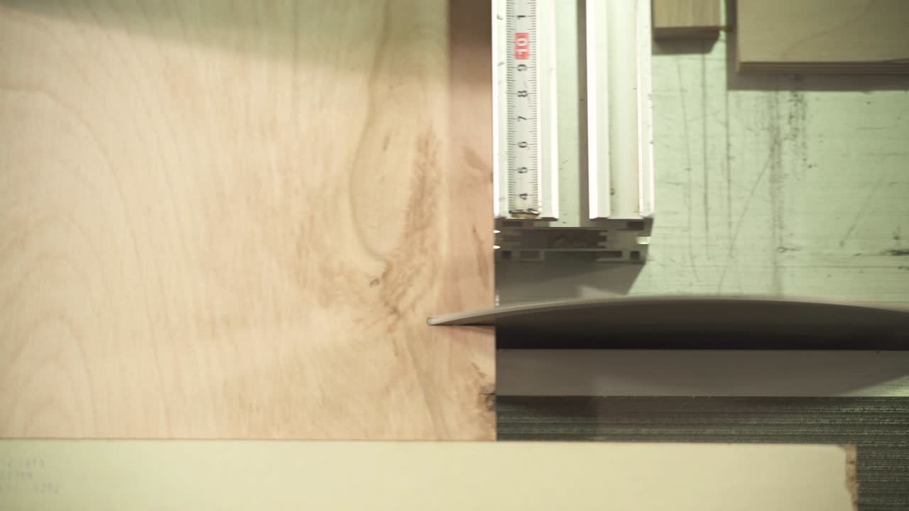una vista superior de una sierra circular de mesa cortando dos piezas pequeñas de una tabla de madera contrachapada en ángulo recto