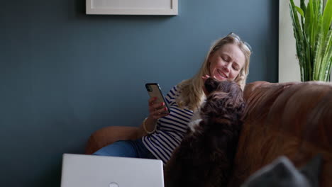 woman relaxing on couch with her dog while using her phone