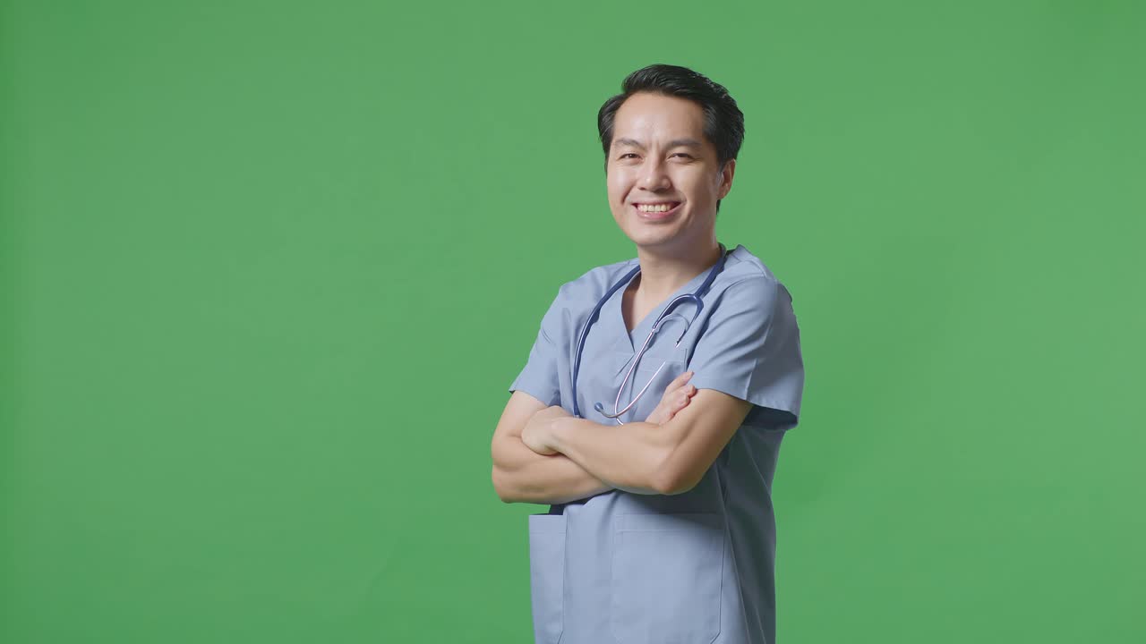 病院の緑の画面の背景に腕を交差させて笑顔を浮かべているステトスコップを持ったアジア人男性医師のサイドビュー