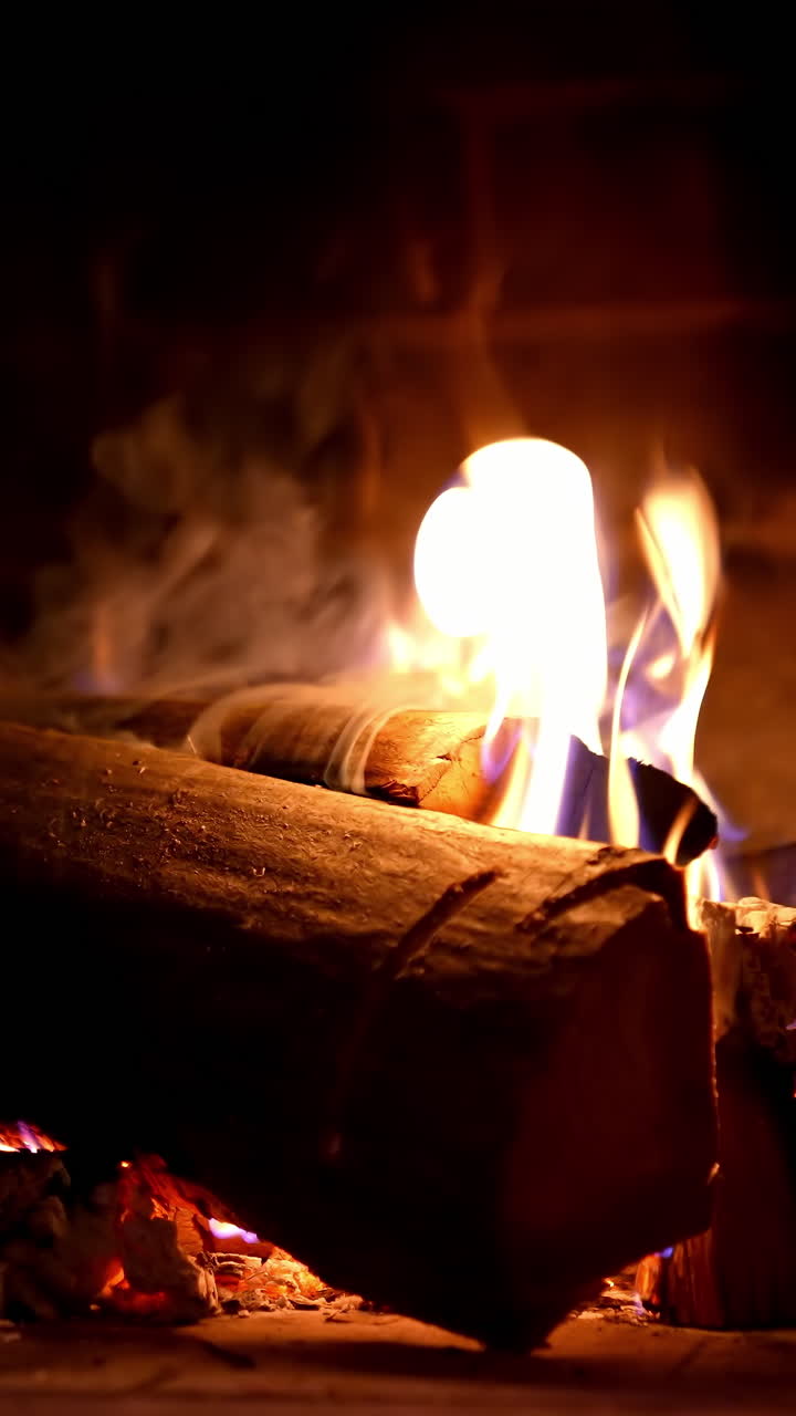 Warmth and comfort at home in cold season. Fire and smoke over wooden logs in fireplace. Wood burning in a stone fireplace. Close-up. Vertical video