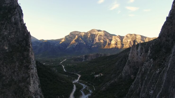 drone flying towards a golden hour mountain ridge on the horizon, river stream in valley, wide sunset aerial shot in Portrero Chico hills, mountains of Hidalgo, Mexico, Nuevo Leon