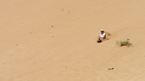 person sandboarding down a desert dune