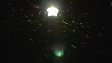 a blizzard casts a heavy snow at night, lit by nothing but a street lamp