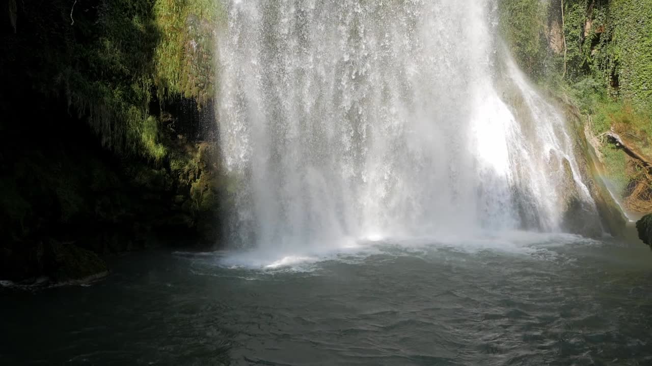Stunning cataract waterfall plunge pool drop of water. Bedrock and vegetation around. Beautiful sunlight and shadow contrast. Colour spectrum from sun rays light reflection. Monasterio de Piedra park
