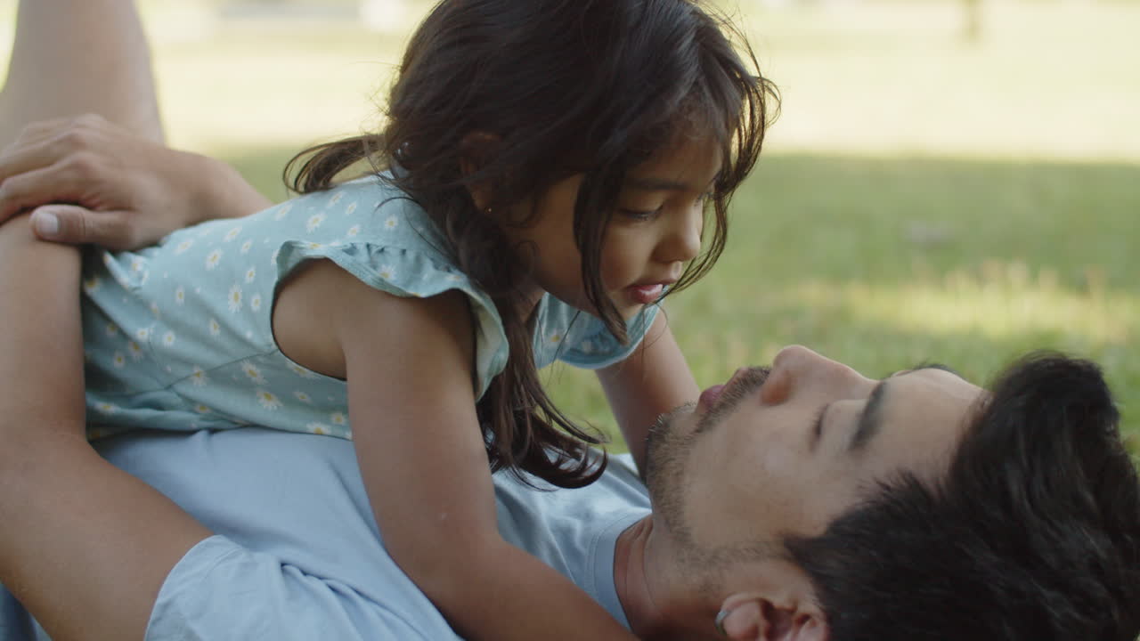 Little girl lying with father on ground and kissing him on lips