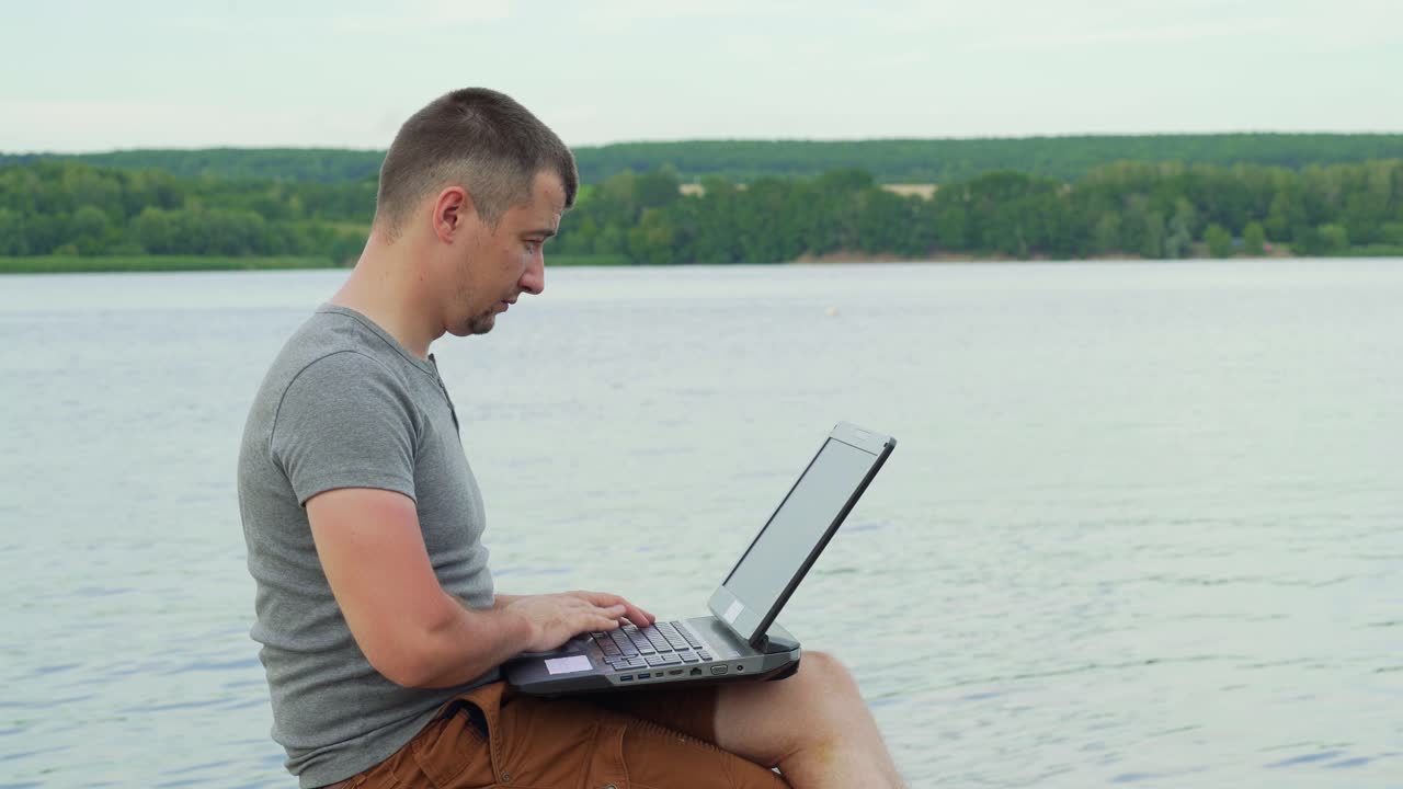 Handsome man sitting on a wooden pier with laptop