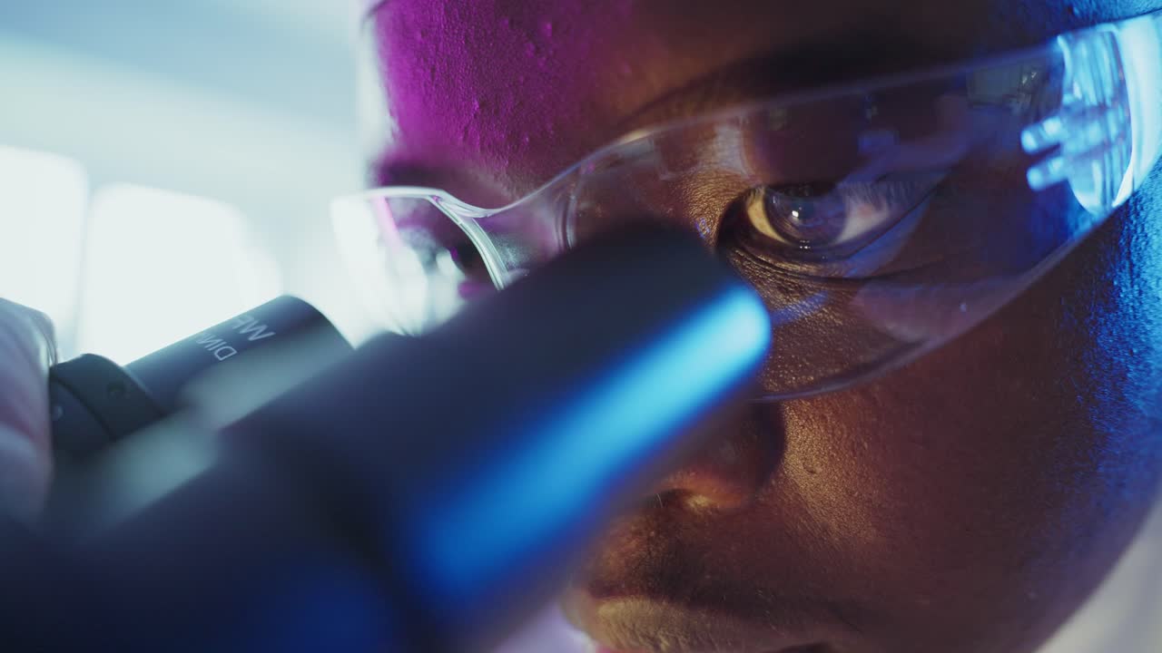 Konzentrierter afroamerikanischer Wissenschaftler schaut durch Mikroskop im Labor