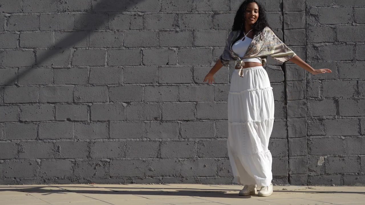 Una donna elegante vestita con un bellissimo abito bianco che posa con grazia contro una parete grigia