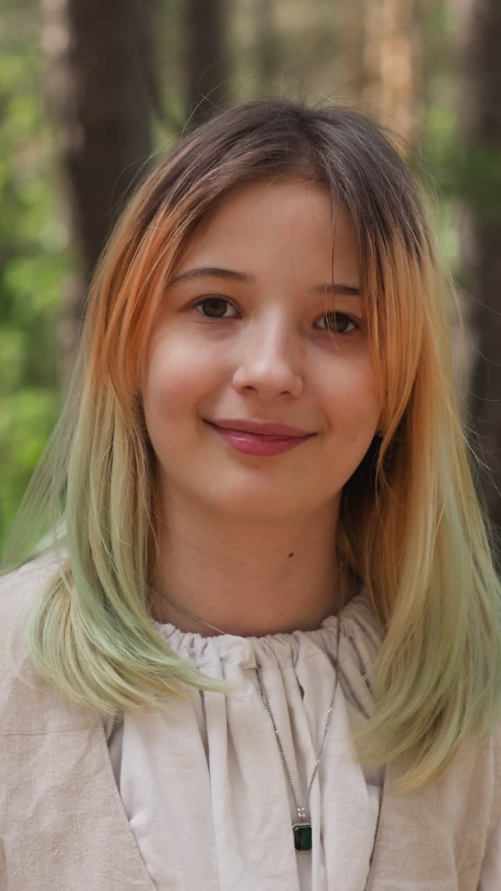 Pretty teenage girl with dyed hair in traditional clothes of medieval period stands in green wood closeup. Young actress at reconstruction filming set