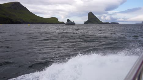 Water-splashes-from-boat-wake,-Drangarnir-and-Tindholmur-islets-in-the-distance-between-Vagar-and-Mykines,-Faroe-Islands