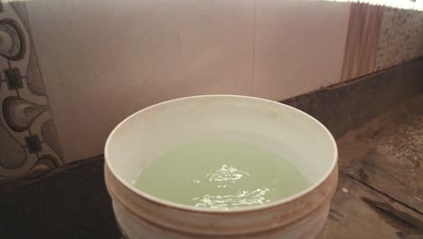 a hand taking out water from a bucket with help of mug