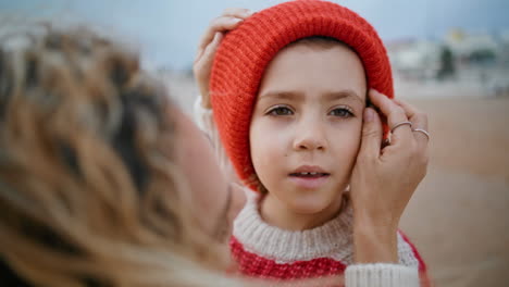 Süßer-Junge-Ruht-Sich-Am-Herbststrand-Mit-Mama-Aus,-Nahaufnahme.-Fürsorgliche-Mutter-Hilft-Mit-Hut