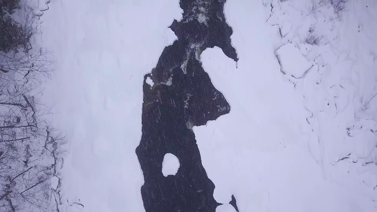 SLOWMOTION OVENFRA af en isnende bæk med en lille sneklædt ø under en snestorm