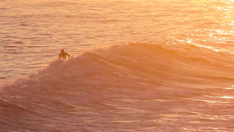 Este-Video-En-Cámara-Lenta-Muestra-A-Un-Surfista-Montando-Una-Ola-Del-Océano-Mientras-El-Agua-Se-Ilumina-De-Color-Naranja-Con-El-Amanecer