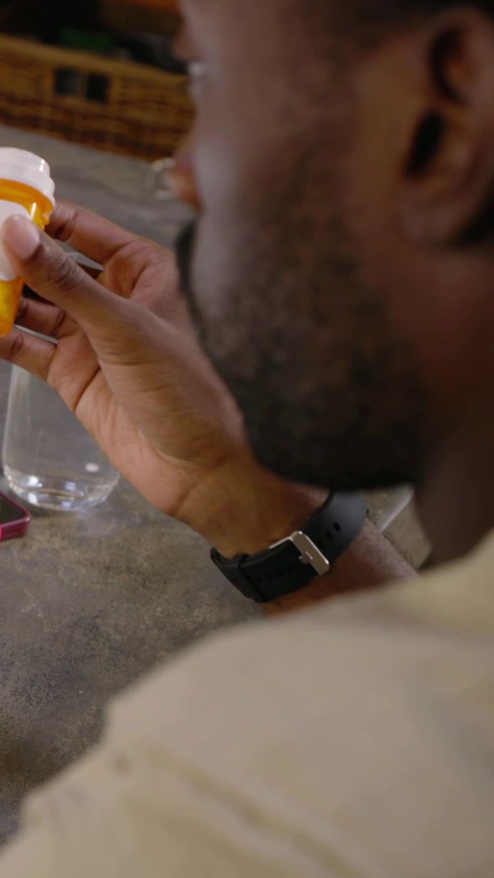 Video verticale: Uomo prende un barattolo bianco, controlla un flacone di pillole arancione e prepara i farmaci sul bancone.