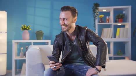 joven carismático y elegante usando teléfono, mensajes de texto, redes sociales en casa.
