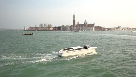 a white vaporetto boat sails from left to right on the waters of the sea, with the city of venice in the background