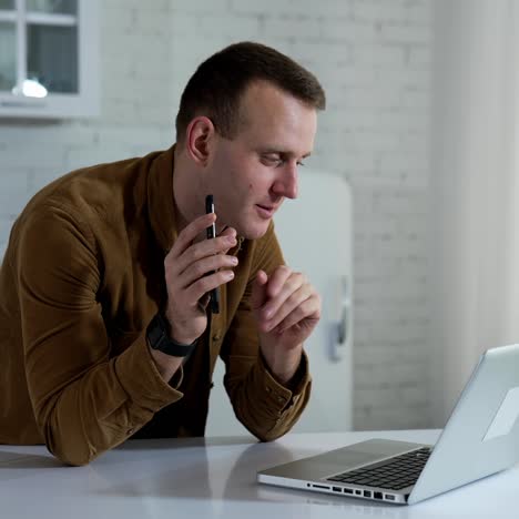 Shopping online. Young man freelancer talking in front of a laptop and proposes new device. Smiling guy working through the laptop computer at home. Remote job