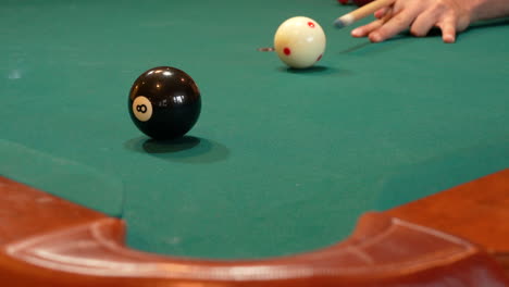 Closeup-of-Person-Playing-Pool-Addressing-and-Shooting-8-Ball-into-Corner-Pocket-after-Practice-Strokes-using-Cue-Ball,-Open-Bridge-Hand-with-Wooden-Cue-Stick,-Solid-Black-Ball-and-Green-Felt-or-Cloth