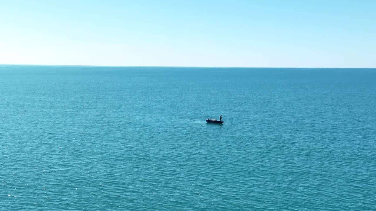 넓은 바다에서 작은 보트에 서 있는 고독한 남자의 공중 정적 샷