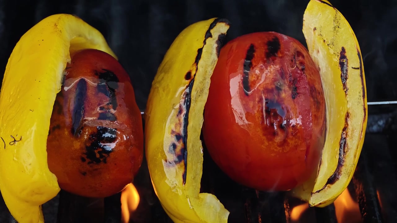Primo piano al rallentatore di spiedino di verdure grigliate con pomodori rossi interi, fette di peperone giallo e olio d'oliva che schizza su una griglia BBQ nera, riprese macro cinematografiche dall'alto di cibo in 4K al tramonto!