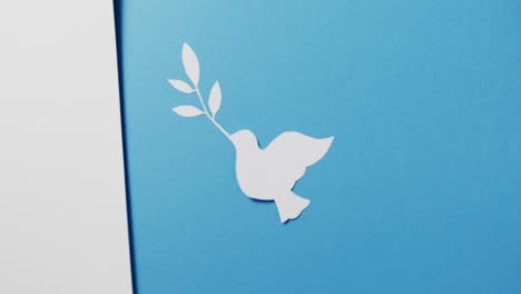 Close-up-of-white-dove-with-leaf,-white-paper-and-copy-space-on-blue-background