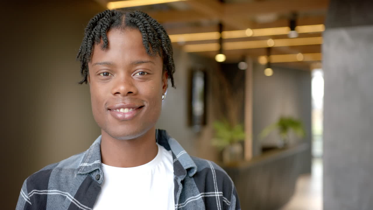 Smiling young man in casual attire standing in modern office hallway