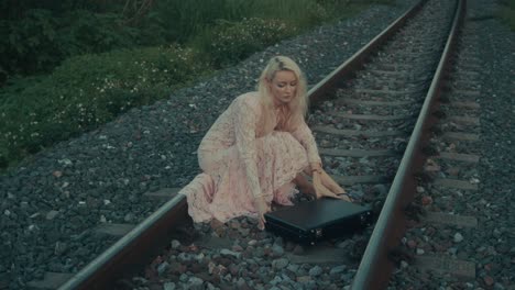 a woman sitting on train tracks with a suitcase
