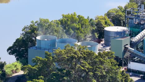drone footage captures cooling towers emitting steam in a lush, industrial setting with clear skies and vibrant greenery