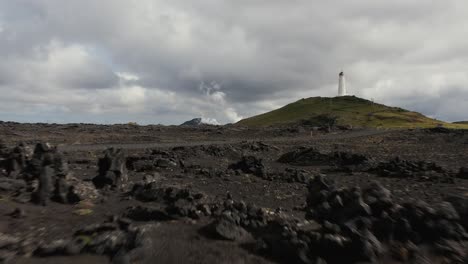 low aerial over rugged volcanic surface with reykjanesviti lighthouse on hill